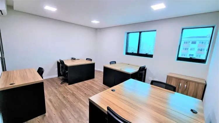 Sala privativa com três estações de trabalho, mobiliário em madeira e vista para a cidade