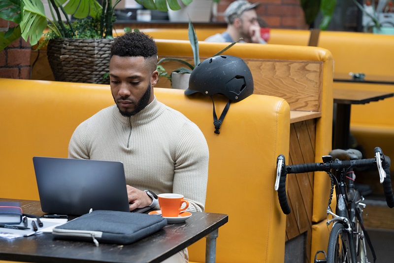 Empreendedorismo digital praticado por um homem sentado no sofá, usando um notebook apoiado sobre a mesa onde há uma xícara laranja.