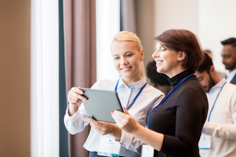 Duas mulheres compartilhando informações sobre tomada de decisões em um tablet durante um evento empresarial.