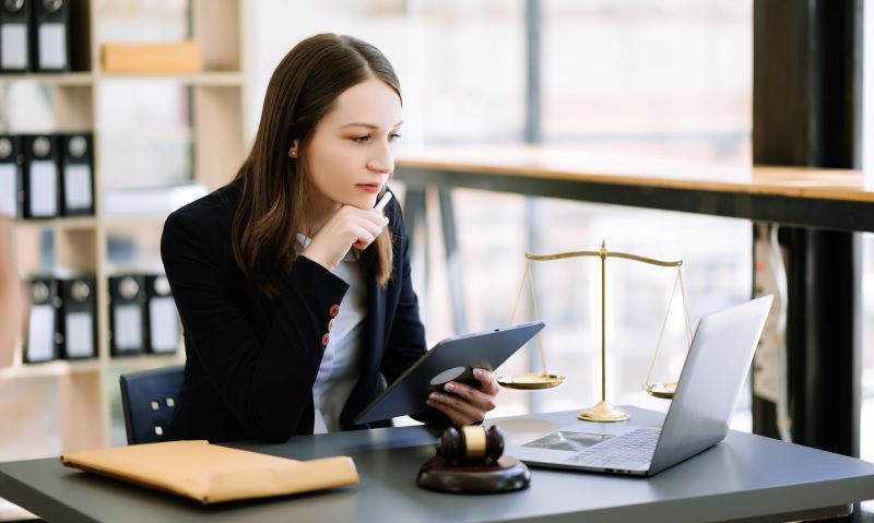 Advogada em escritório com tablet em mãos e notebook na mesa, lendo sobre como captar clientes na advocacia.