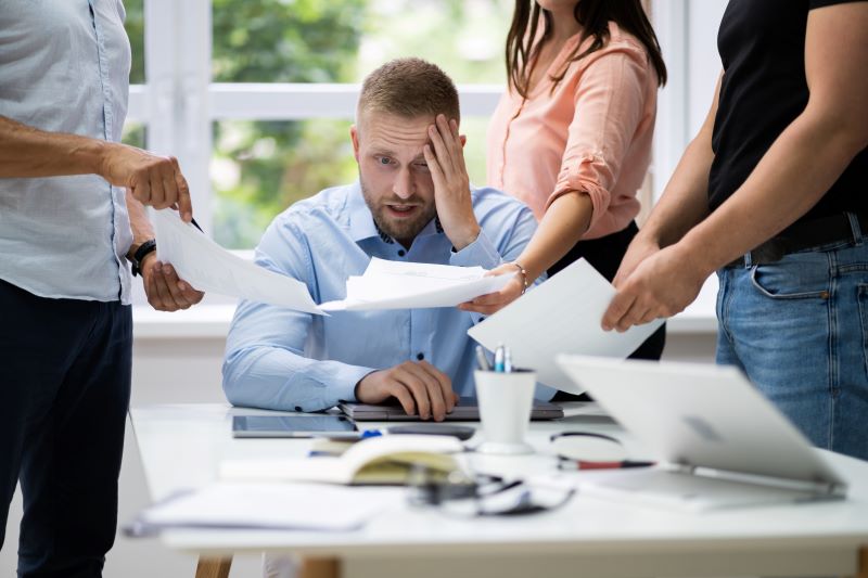 Várias pessoas entregam demandas para trabalhador estressado que tem dificuldade devido à comunicação passiva.