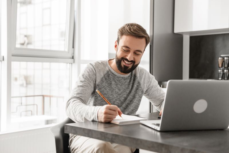 Homem em casa no computador anotando 7 ideias de negócio para começar com pouco dinheiro.