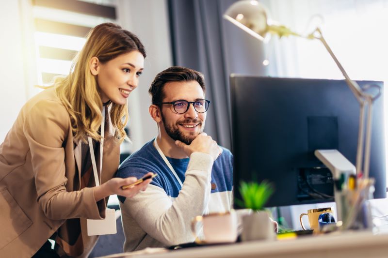 Mulher e homem trabalhando em uma startup enxuta sorriem enquanto estão vendo algo no computador.