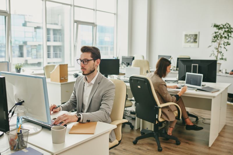 Impostos municipais​: duas pessoas trabalhando em coworking, de costas uma para a outra.